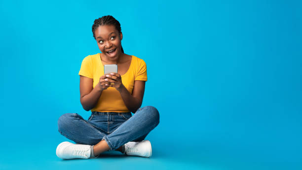 istock Positive African Girl Using Smartphone Sitting Over Blue Background, Panorama 1256670565