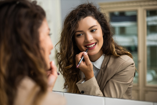 Businesswoman is applying  lipstick while preparing for work.