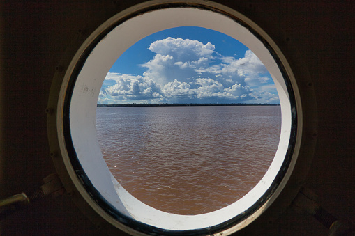 View through a ship's porthole of the Amazon River with a bank of Cumulus cloud overhead, in Para State, Brazil. March 29 2018