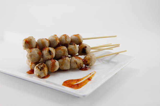 Meatballs on skewers put in a white bowl topped with delicious dipping sauce.  Located on a white background.