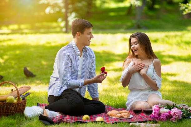 istock Romantic young man making proposal to his surprised girlfriend on picnic at park 1256676650