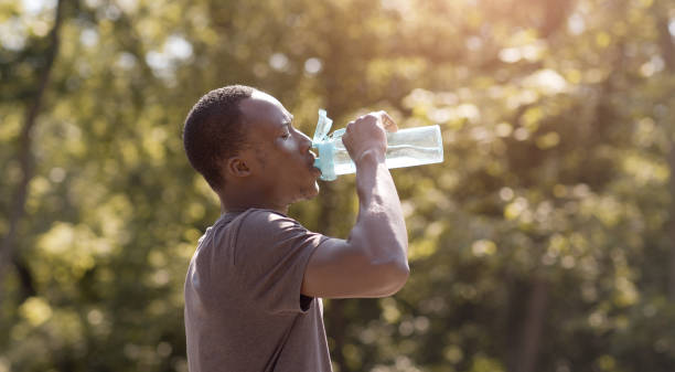 ragazzo nero surriscaldato che beve acqua dalla bottiglia nel parco - water bottle water bottle drinking foto e immagini stock