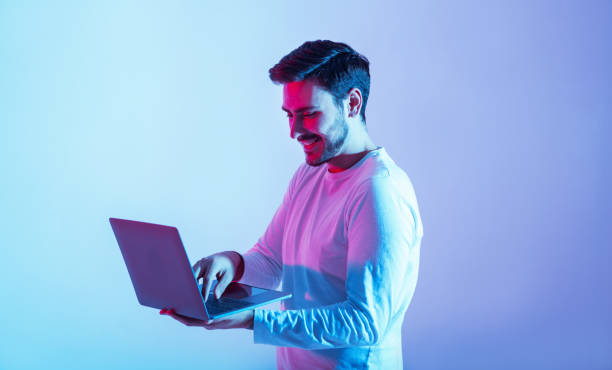 istock Work and play online. Happy guy holding laptop and typing 1256676934