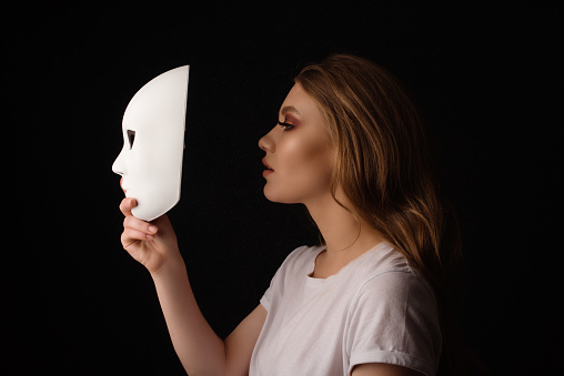 Profile view of blond woman holding white mask acting out and pretending, feeling depressed