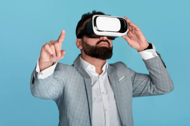 istock Businessman wearing virtual reality headset and pointing at imaginary screen over blue background 1256678312