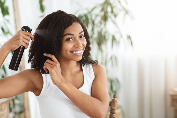 Hairstyling. Smiling Black Woman Applying Texturising Spray To Her Beautiful Curly Hair Hairstyling. Smiling Black Woman Applying Texturising Spray To Her Beautiful Curly Hair At Home, Getting Ready To Go Out, Copy Space combing photos stock pictures, royalty-free photos & images