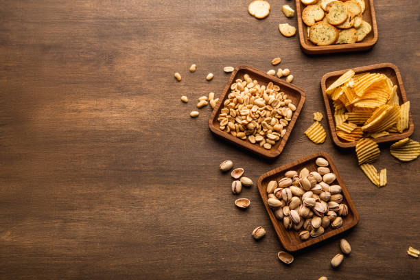Crispy snacks on background. Pistachios, nuts, crisps and chips in plate and scattered on table Crispy snacks on background. Pistachios, nuts, crackers, crisps and chips in plate and scattered on wooden table, top view, free space pub table top view stock pictures, royalty-free photos & images