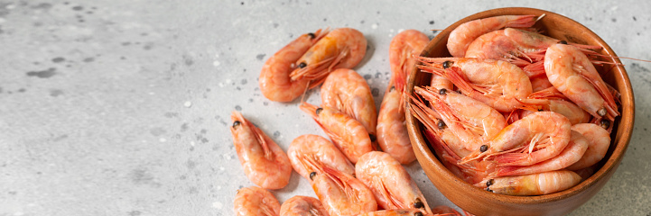 Prawns in a wooden bowl on a light gray table. Lots of shrimp in a bowl. Shrimp close-up. Top view with space for text. Banner