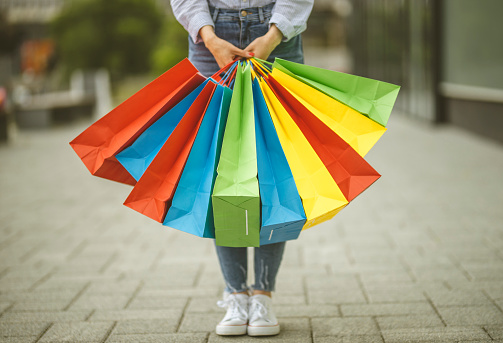 Close up of unrecognizable person holding colorful shopping bags and standing
