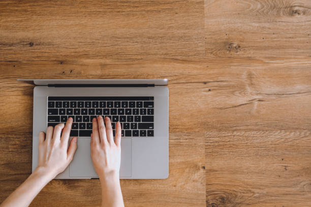istock Female hands are typing in a notebook keyboard on a wooden background 1256686306