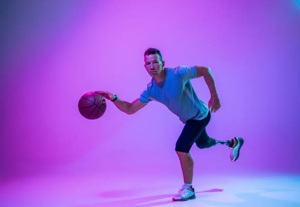 istock Athlete with disabilities or amputee isolated on gradient studio background. Professional male basketball player with leg prosthesis training and practicing in studio. 1256690739