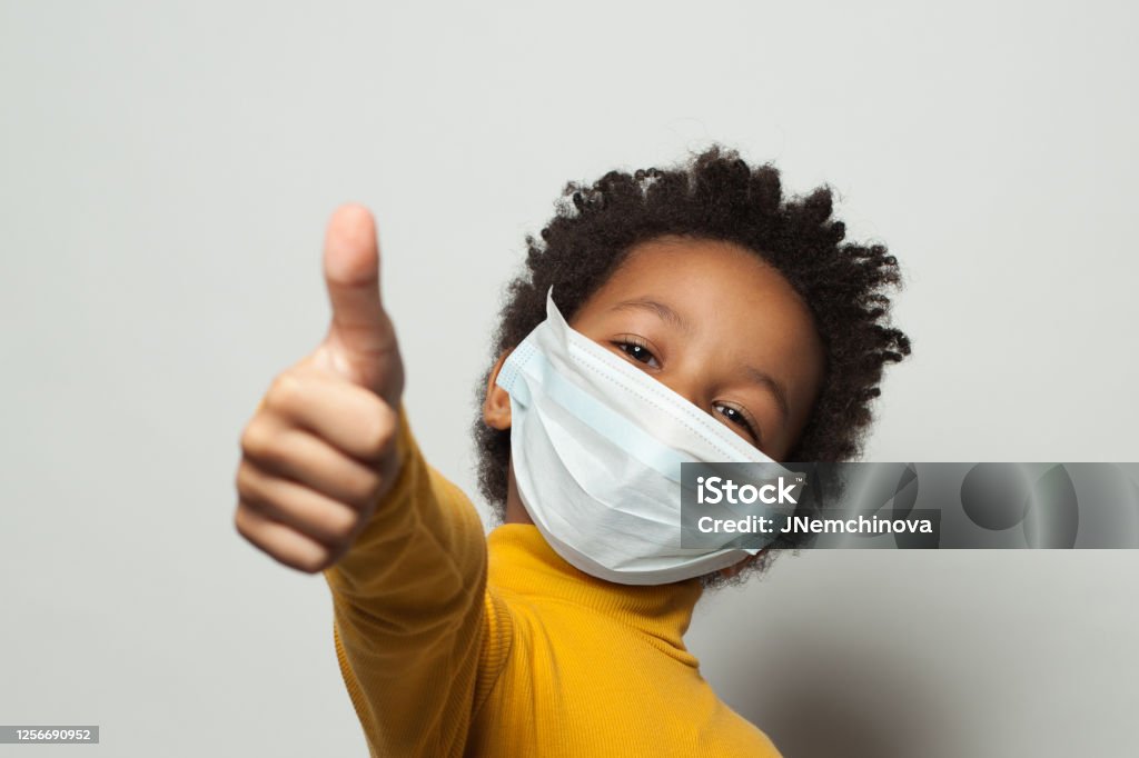 Feliz niño negro afroamericano con máscara de la cara protectora médica que muestra el pulgar hacia arriba en blanco - Foto de stock de Niño libre de derechos