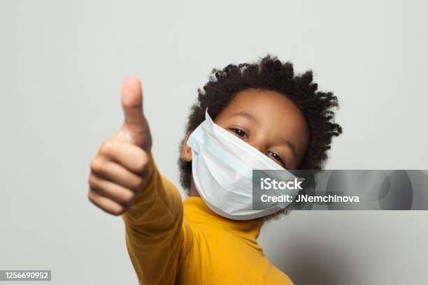 Feliz Niño Negro Afroamericano Con Máscara De La Cara Protectora Médica Que Muestra El Pulgar Hacia Arriba En Blanco Foto de stock y más banco de imágenes de Niño