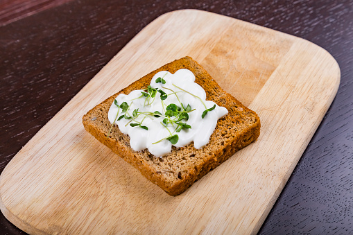 Sandwich with cream cheese and fresh basil microgreen sprouts on cutting board. Healthy eating, diet vegan food background. Top view.