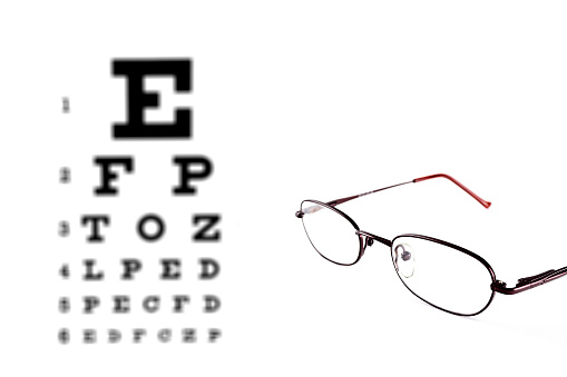 Black, eyeglasses on top of an eye chart.