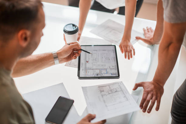 Creative team of architects designers discussing ideas, working with tablet in modern office