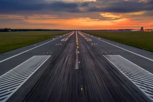 Photo of Used concrete asphalt airport empty runway with many braking marks, markings for landings and all navigation lights on. Clear for comercial airplane landing or taking off in Wroclaw airport
