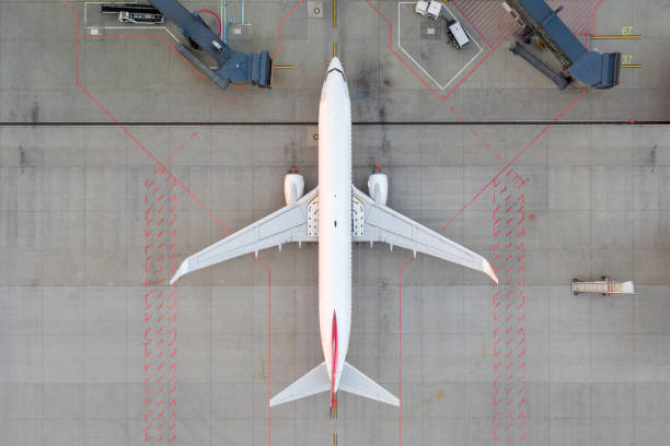 Top down view on comercial airplane docking in terminal in the parking lot of the airport apron, waiting for services maintenance, refilling fuel services after airspace lock down. Modern airliner Top down view on comercial airplane docking in terminal in the parking lot of the airport apron. Modern airliner taxiway stock pictures, royalty-free photos & images