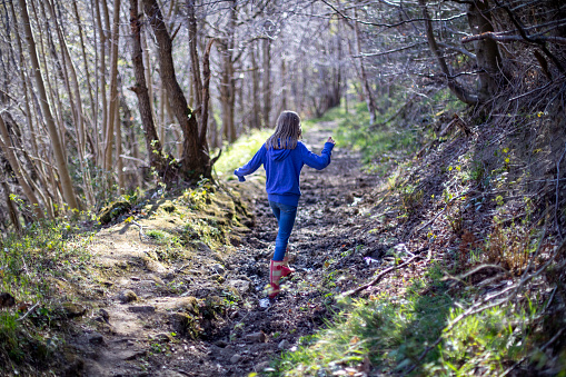 A shot of a young, unrecognisable girl walking through a muddy path in a forest in Northumberland, Northeastern England.