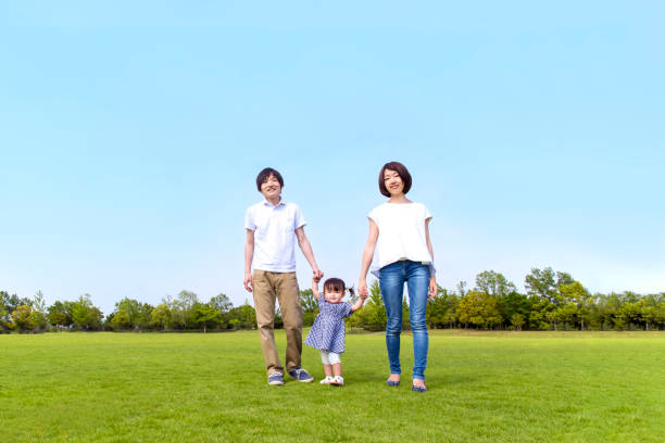 Parents and little daughter walking on green grass square against blue sky Parents and little daughter, walking, green grass square, blue sky, camera eye, happy family embankment photos stock pictures, royalty-free photos & images