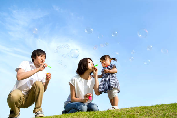 Parents and little daughter playing with soap bubbles against blue sky