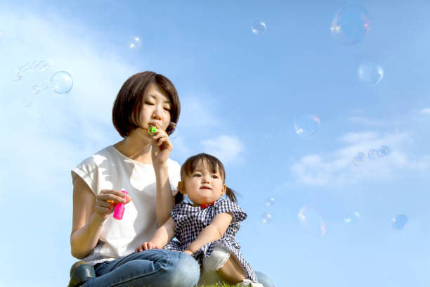 istock Mother and little daughter playing with soap bubbles against blue sky 1256701164