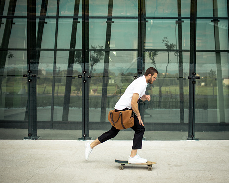Hipster businessman riding skateboard on his way to work. He is in front of modern building