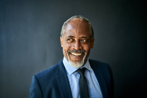 istock Smiling mature businessman standing against a black background 1256712764