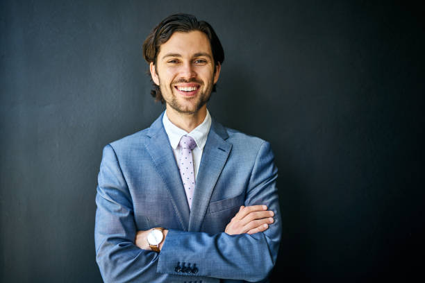 istock Smiling young businessman standing against a black background 1256712884
