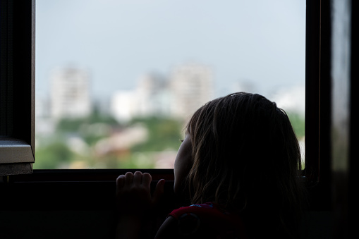 silhouette of a sad child leaning on the edge of an open window and looking into the distance