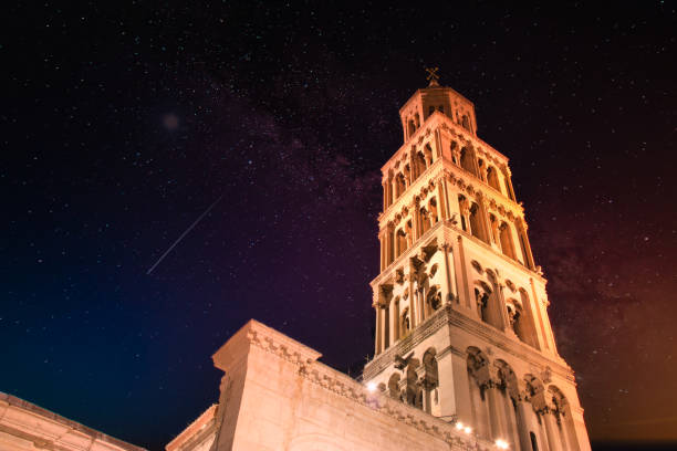 Saint Dominus belltower seen from below, long exposure, illuminated by orange lights at night, beautiful colorful night sky with purple and orange colors