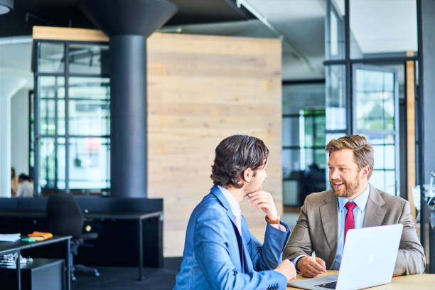 istock Two smiling businessmen working on a laptop in a modern office 1256719576
