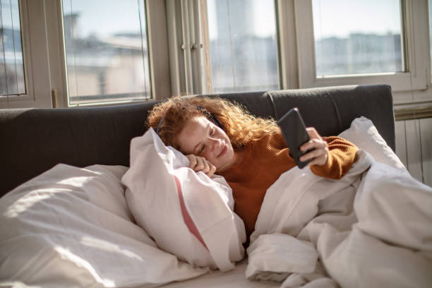 istock Young woman using a mobile phone in bed 1256719620