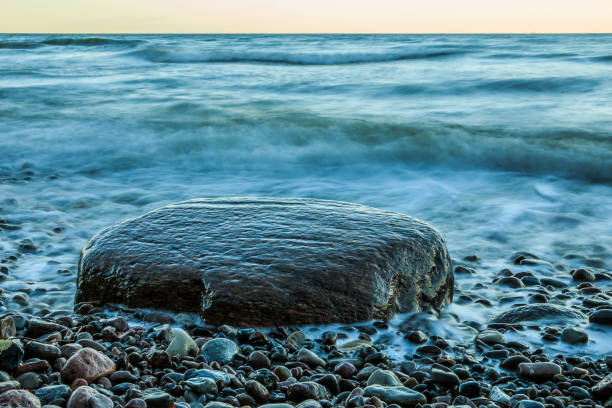 Baltic coast in the morning after sunrise. Large stone in the foreground on the stony stretch of beach. Light waves on the coast of Ruegen Island