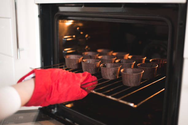 Woman put batter for chocolate cupcakes in oven in kitchen closeup. Cooking time.