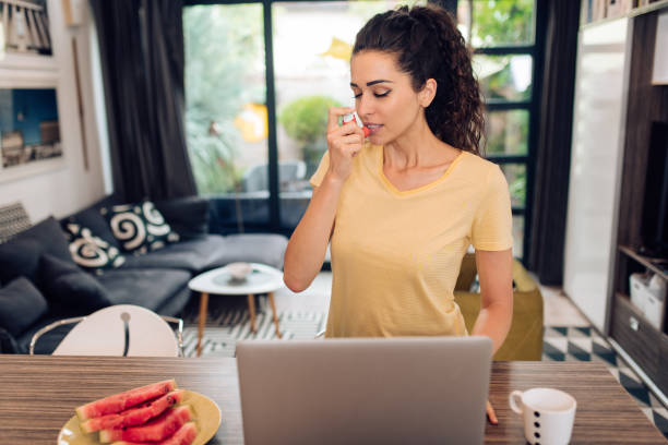 istock Young woman using asthma inhaler while working from home office 1256725639