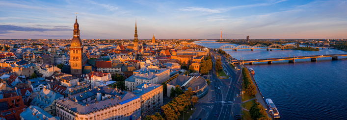 Flying over beautiful old town of Riga, Latvia at sunset with Domes cathedral and golden cock statue in the foreground.