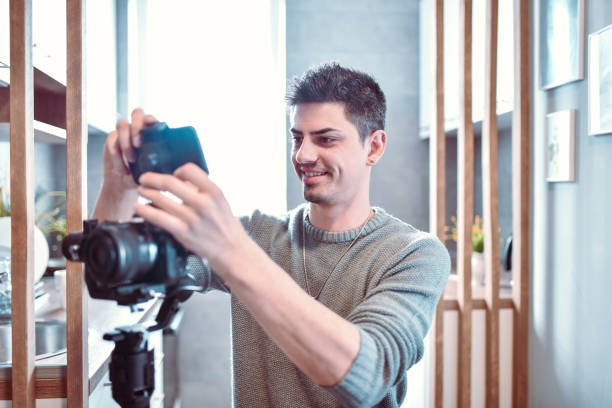 istock Smiling Male Ready To Record Video With Camera At Home 1256731976
