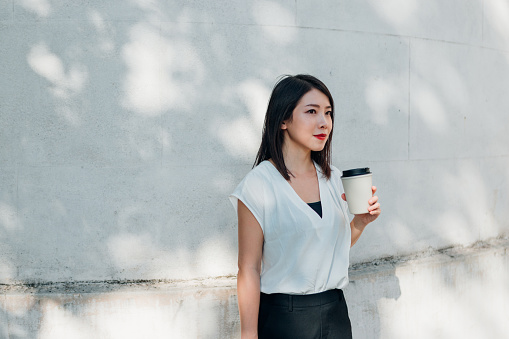 Shot of a young Asian beautiful businesswoman having coffee in reusable coffee cup and taking a break in the city