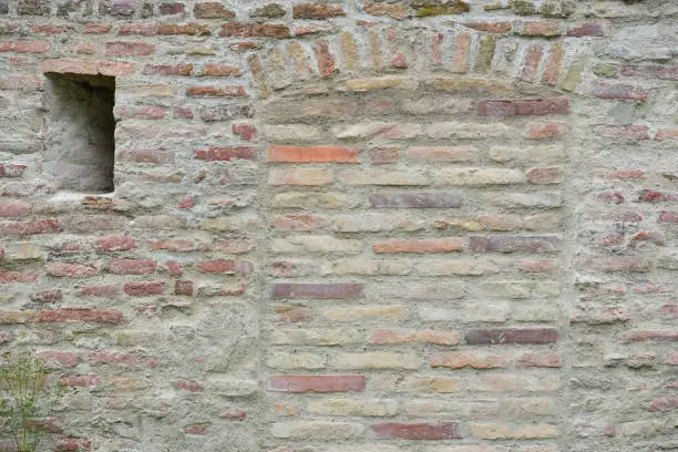 an old wall made of burnt bricks, with a bricked-up door and a loop hole on the side