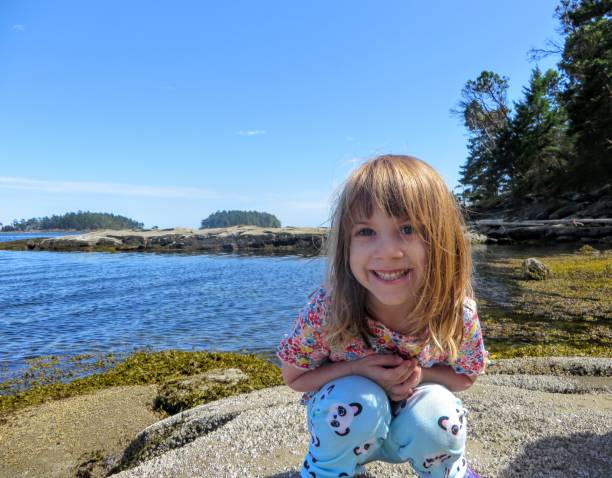 A happy girl smiling for the camera as she explores the coast of the gulf islands in British Columbia, Canada. stock photo