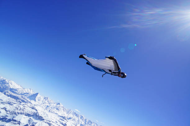 le costume d’aile s’élève au-dessus du paysage de montagne - wingsuit photos et images de collection