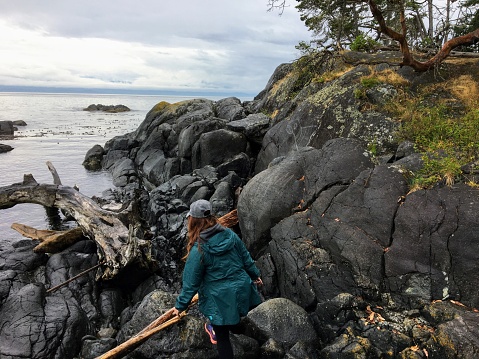 Beautiful photo of a woman hiking a picturesque rocky shoreline surrounded by the vast ocean and first nations petroglyphs, along the east sooke coast trail in British Columbia, Canada