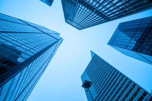 Converging high-rise commercial office buildings in blue hues towering skyward from street level.