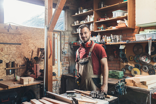 Smiling young man in his furniture workshop, small business concept.