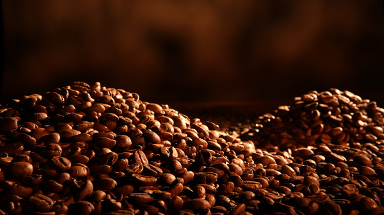 Two large piles of roasted Coffee Beans on Brown background in warm Dramatic lighting