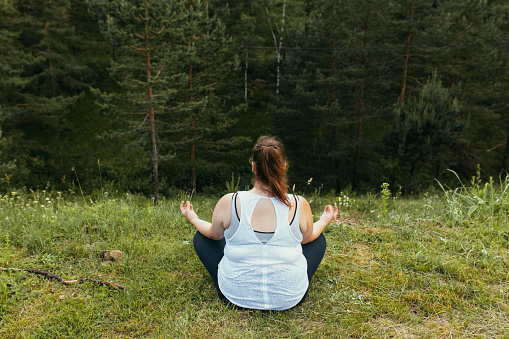 Curvy woman relaxing by doing yoga in nature.