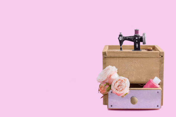 Vintage wooden box  for storing sewing supplies with miniature sewing machine,  a spool of thread and  three buds of rose. Close up. Copy space.
