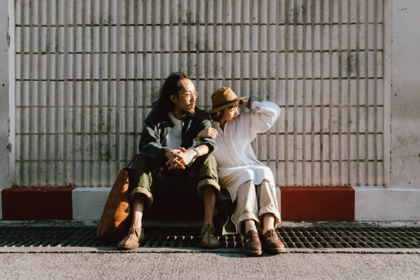 Full length of upset young couple sitting back to back on chairs against gray background