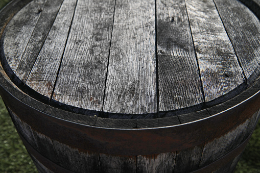 Wooden top of old weathered wine barrel stands outside.